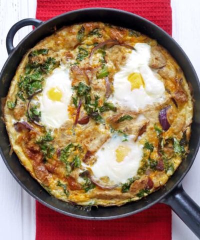 chorizo and kale strata in a black frying pan sat on a red place mat.