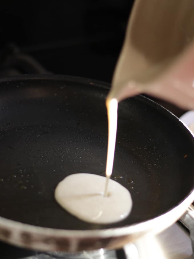 Pouring pancake batter into a black frying pan.