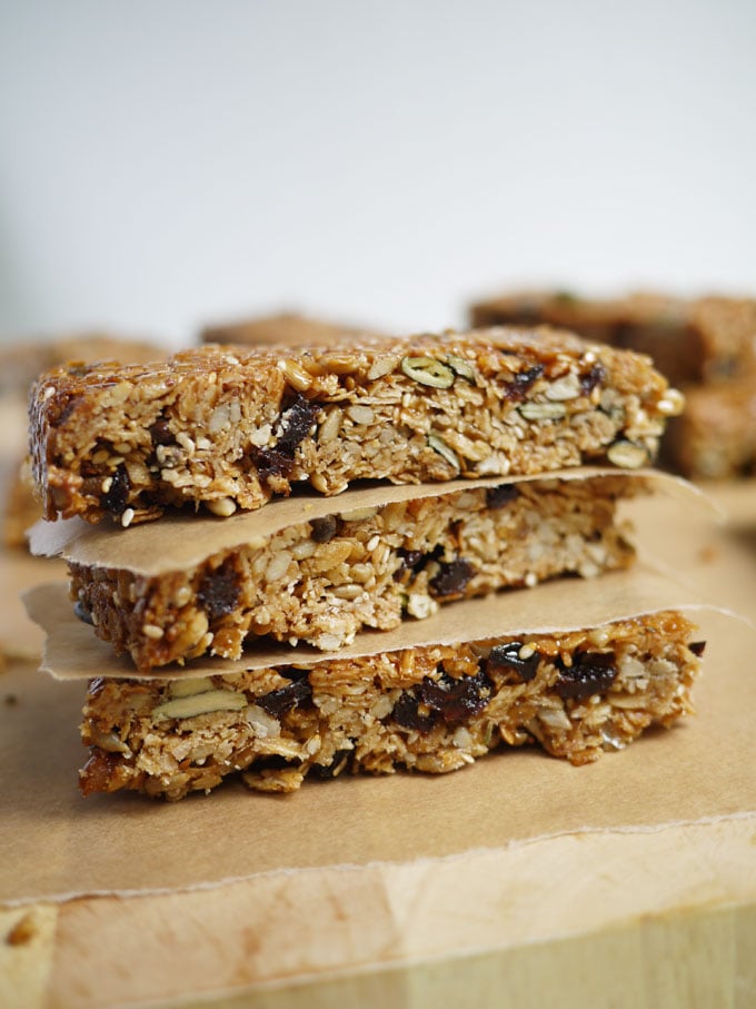 three homemade granola bars full of seeds and dried fruit stacked on wooden board