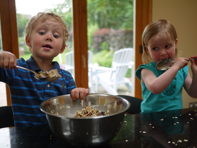 toddler boy and girl spooning ingredients for homemade granola from silver bowl.