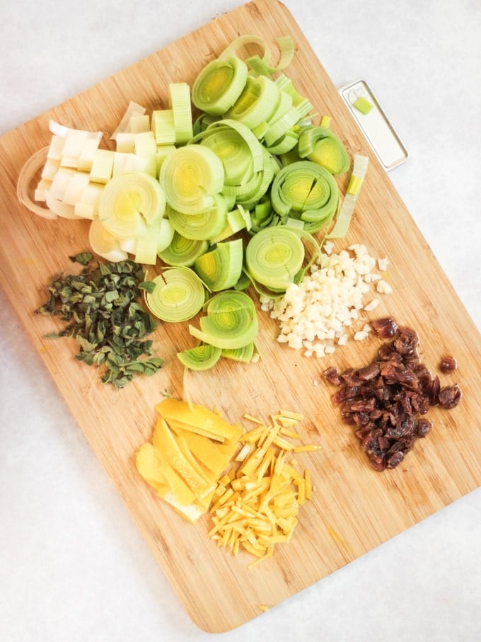 Leeks, anchovies, lemon zest, oregano and garlic chopped on a chopping board