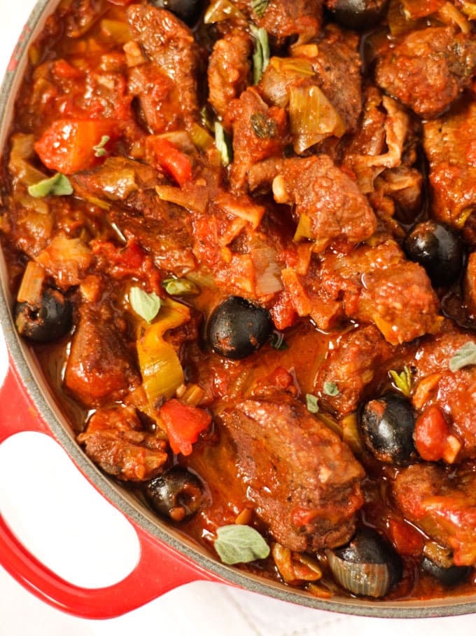 Greek pork casserole in a le creuset pan with olives and oregano