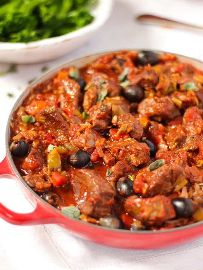 Pork casserole in a red dish with tender stem broccoli and orzo pasta in background