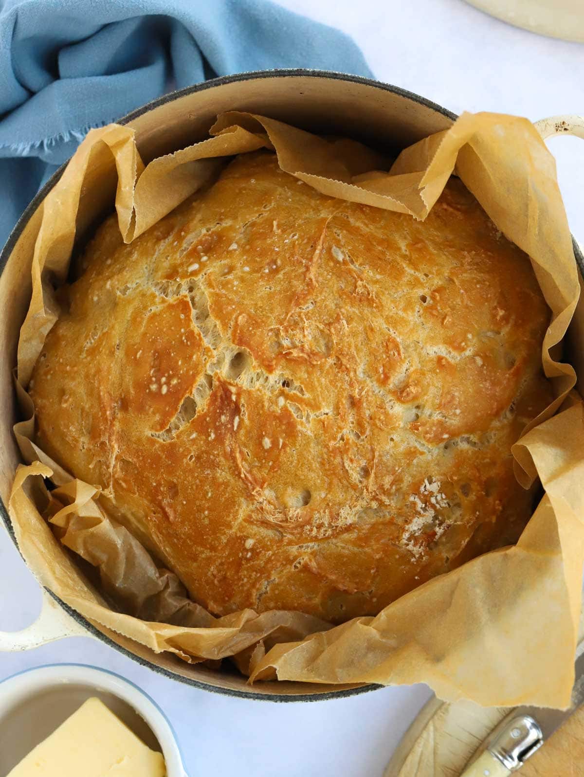 Looking down on a golden brown homemade loaf in a pan with baking paper for the recipe No Knead Bread.