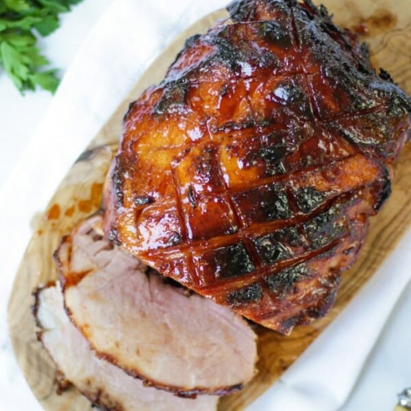 Overhead photo of finished joint of slow cooker ham on a wooden board with a white napkin, a bunch of parsley and two slices cut off.