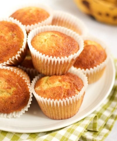 Banana muffins on a plate piled up with ripe bananas in the background