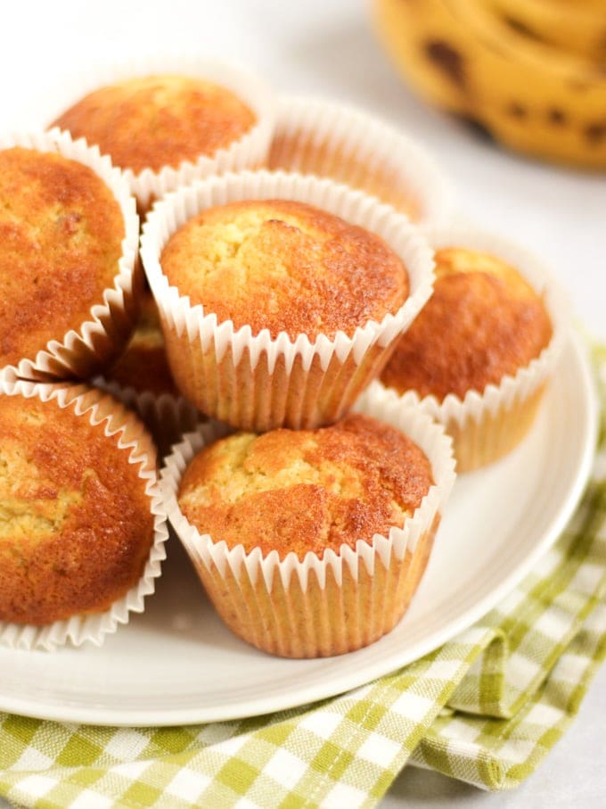 Banana muffins on a plate piled up with ripe bananas in the background