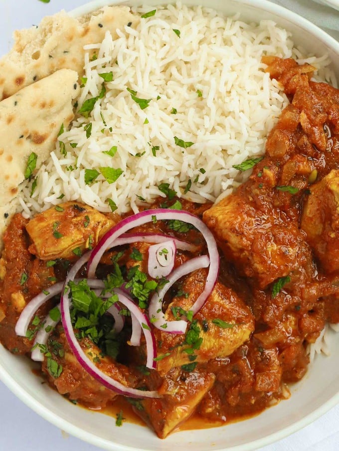 A bowl filled with tasty and healthy chicken curry, white rice and a bit of naan bread.