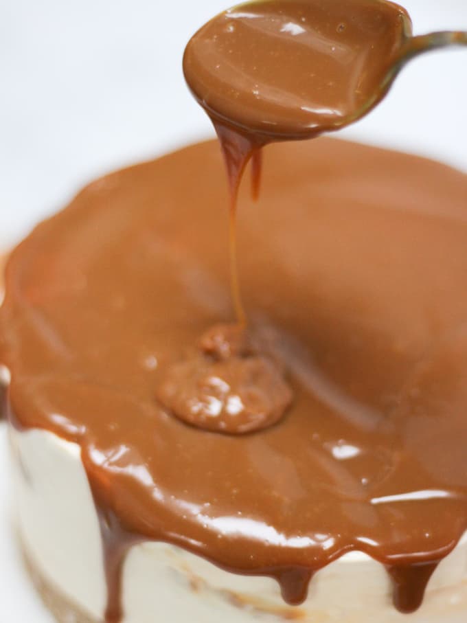 Drizzle and spoon of caramel for no bake salted caramel cheesecake on white background.