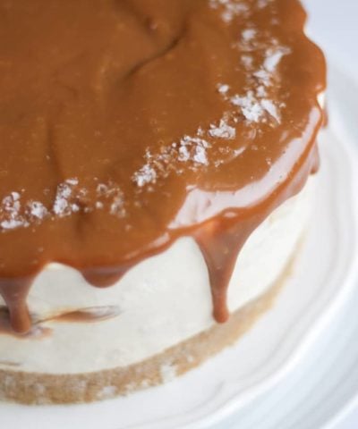 Side view of salted caramel cheesecake with dripping caramel on a white plate.