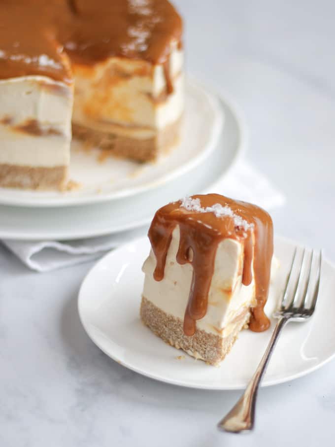 Slice of salted caramel cheesecake with caramel dripping down the edge of the slice on a white plate with fork.