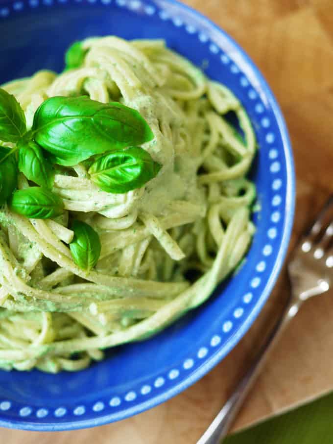 Slimming World pesto on linguine pasta with basil leaf in a blue bowl overhead with a fork on wooden background.