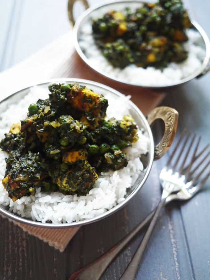 Two bowls laid on a table filled with white rice and Palak Paneer curry on top. Two forks are at the side.