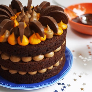 three tier chocolate orange cake with orange buttercream decorated with terrys chocolate orange on a blue plate