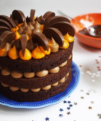three tier chocolate orange cake with orange buttercream decorated with terrys chocolate orange on a blue plate