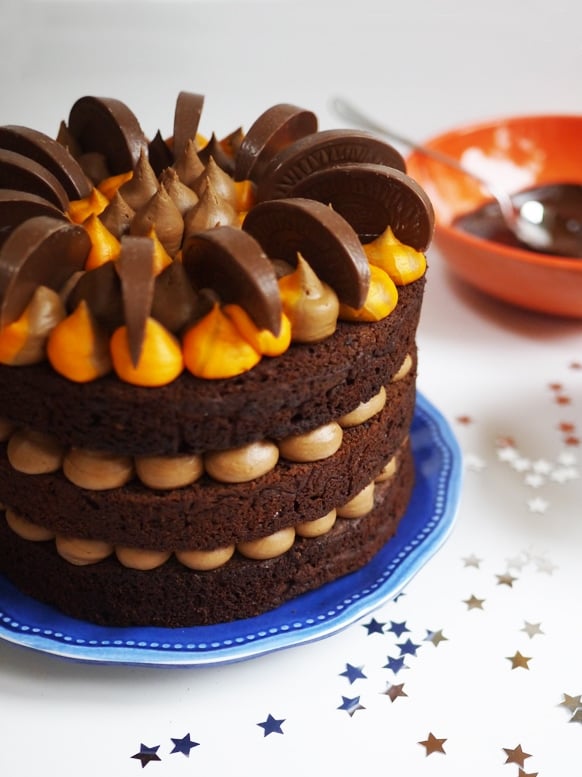 Chocolate orange layer cake piped with chocolate and orange buttercream and chocolate orange Terry's segments on a blue plate.