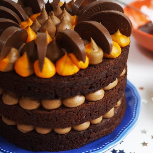 A layered chocolate orange cake with decorative buttercream icing and segments of Terry's Chocolate Orange on top. Served on a plate on a table decorated with small stars.
