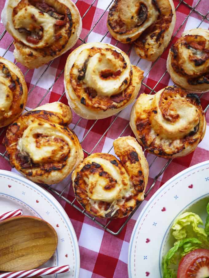 A wire rack on a red and white tablecloth with just-baked Pizza Rolls on top, with side salad on a plate.