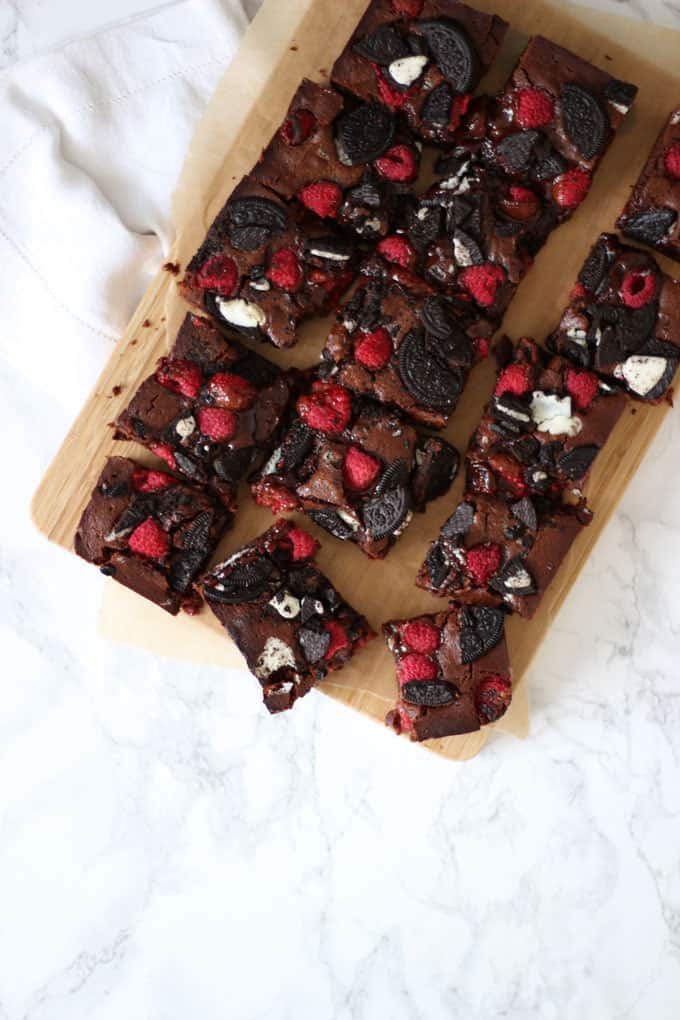 Oreo brownies with raspberries cut into squares on a wooden chopping board and a marble background.