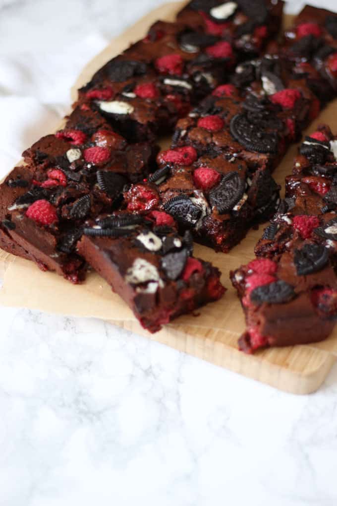 Side angle of gooey Oreo brownies with raspberries on a wooden board on a marble background,
