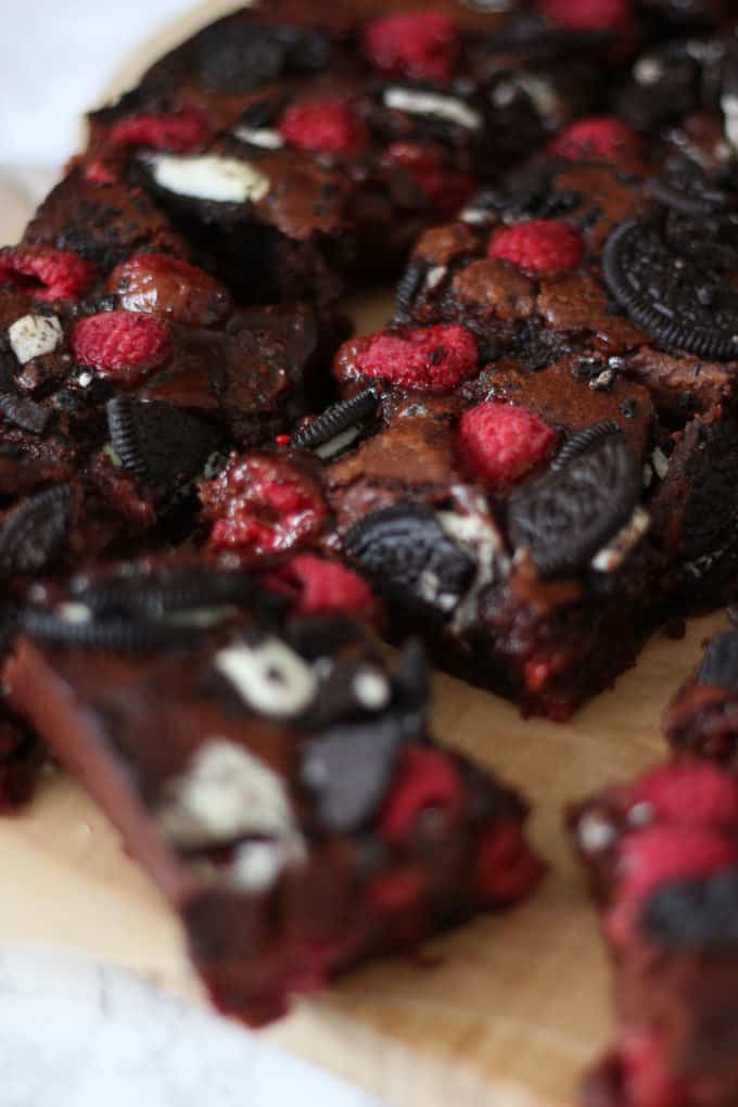 Close up or Oreo Brownies with Raspberries cut into squares on a wooden background.