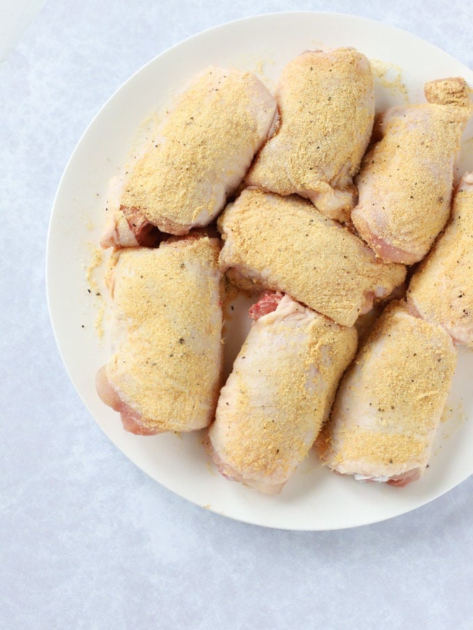 Raw chicken thighs on a plate rubbed with garlic powder.