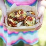Mini Crustless Quiches with Cherry Tomatoes in a lunchbox lined with baking paper held in the hands of a little girl.