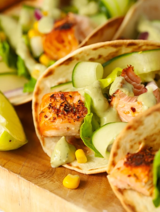 Easy salmon tacos recipe on a wooden board with cucumber and avocado dressing.