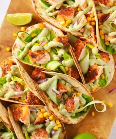 Easy salmon tacos recipe on a wooden board with cucumber and avocado dressing