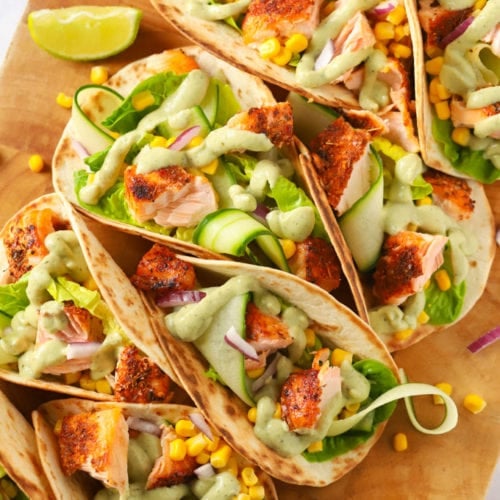 Easy salmon tacos recipe on a wooden board with cucumber and avocado dressing.