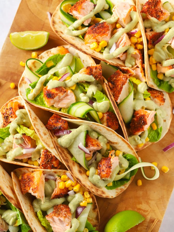 Easy salmon tacos recipe on a wooden board with cucumber and avocado dressing.