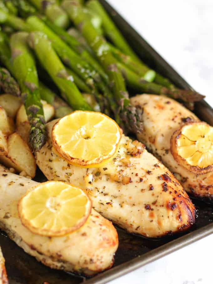 oven baked chicken fillets topped with lemons and asparagus on a grey baking tray