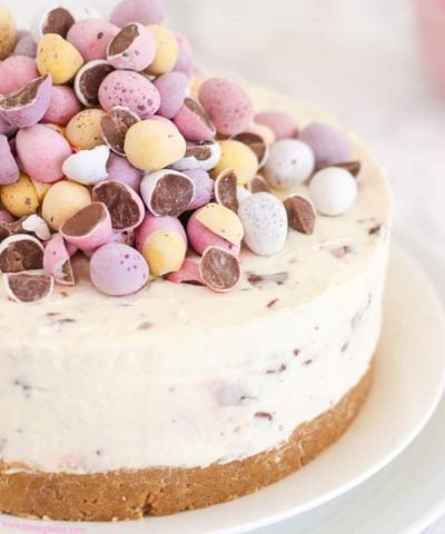 Cheesecake topped with pastel coloured candy eggs on a white plate.
