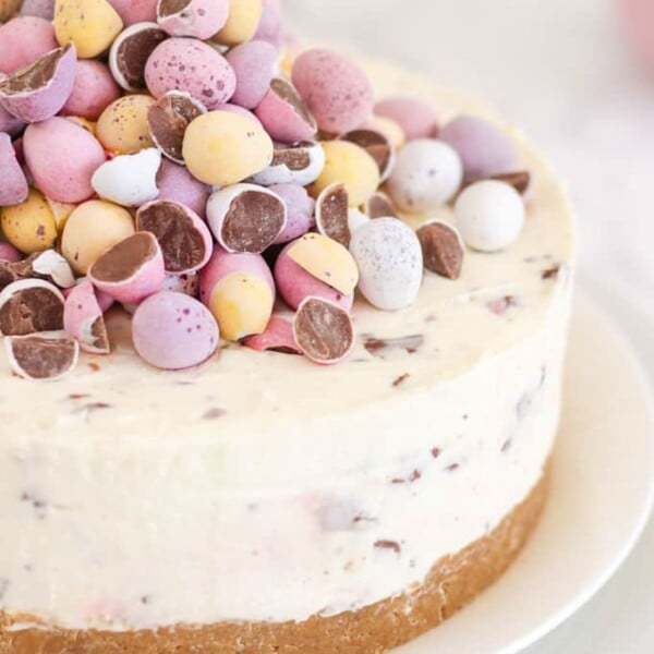 Cheesecake topped with pastel coloured candy eggs on a white plate.