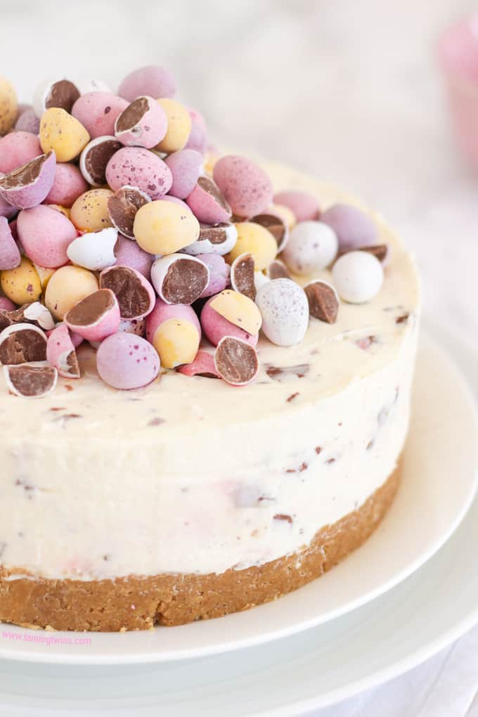 Cheesecake topped with pastel coloured candy eggs on a white plate.