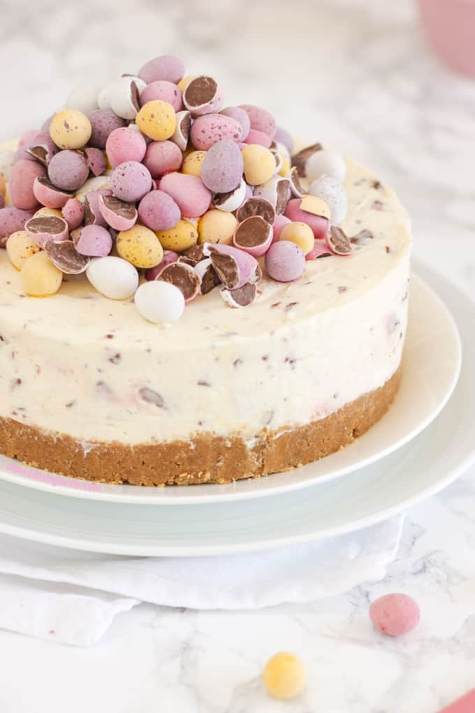 Side view of mini egg piled topped cheesecake on two white plates.