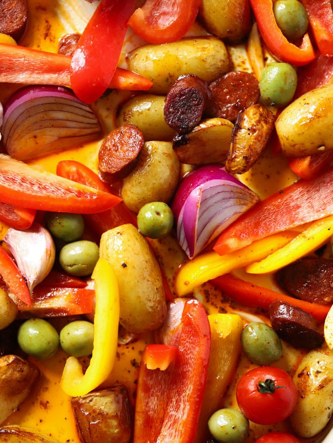 Roasted peppers, chorizo and onions with olives on a baking sheet.