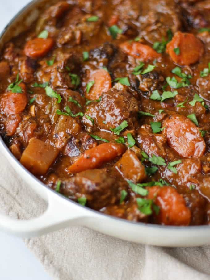 Side angle view of almond le creuset dish full of beef Guinness stew sprinkled with parsley.