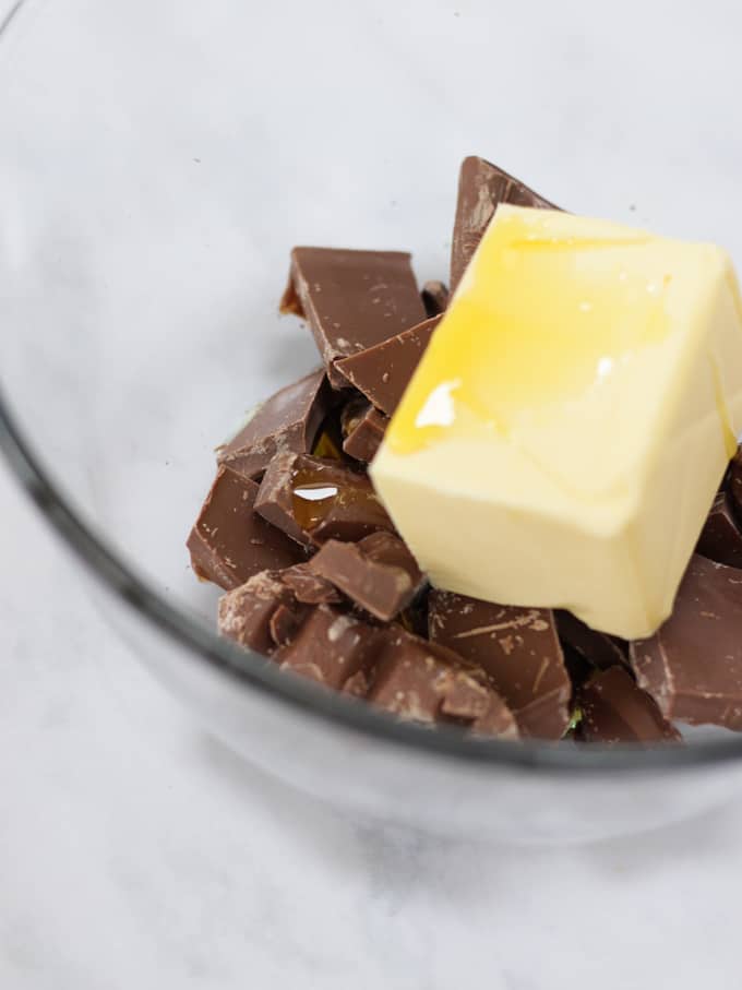 A glass bowl with chocolate chunks, a block of butter and golden syrup in.