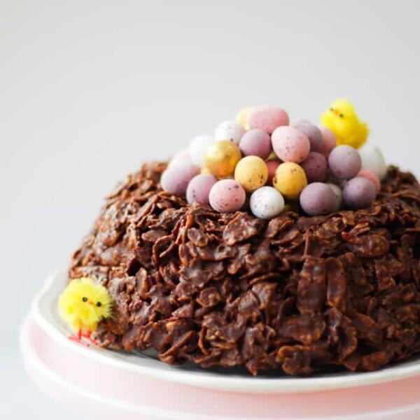 Easter chocolate cornflake cake giant next with mini eggs and Easter chicks on a pink stand. side view.