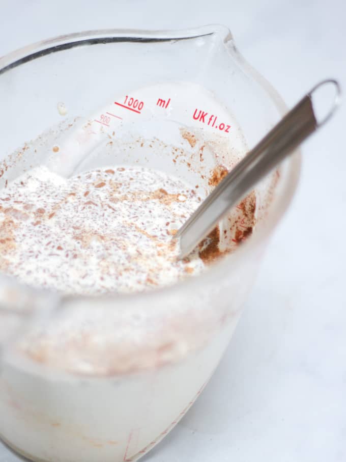 Measuring jug filled with milk and cinnamon on a white background.
