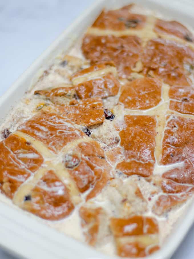 Hot cross bun bread and butter pudding recipe soaking before baking in a cream coloured Le Creuset dish.
