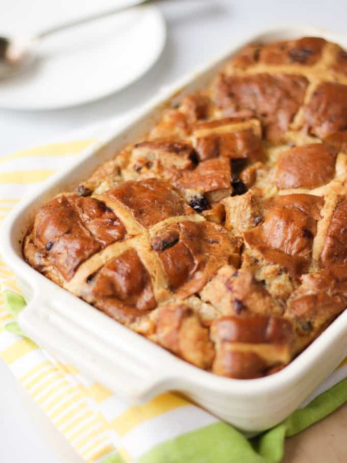 Side angle view of a hot cross bun bread and butter pudding on a yellow and green stripe tea towel.