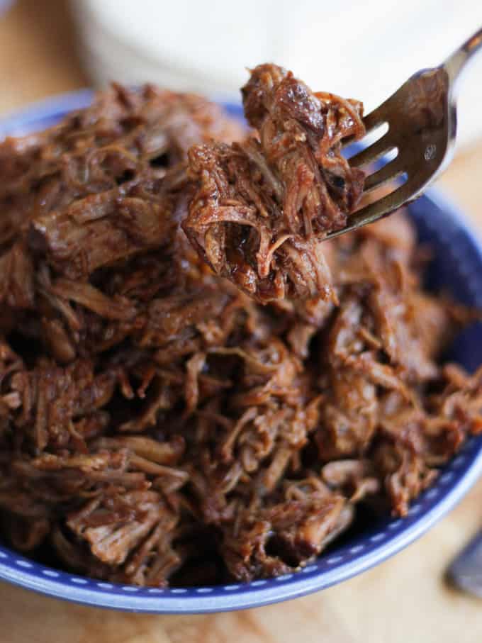 Instant pot pulled pork in a blue bowl being lifted on a fork.