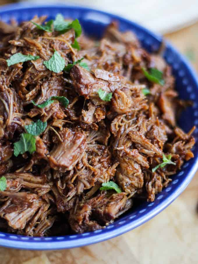 Side view of instant pot pulled pork sprinkled with mint in a blue bowl.