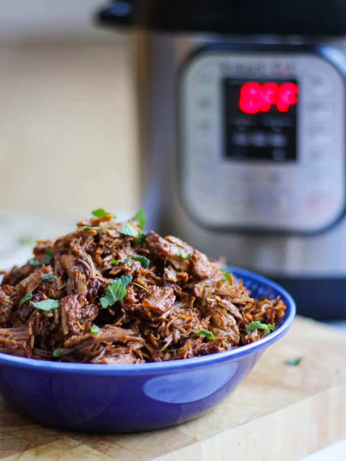 Blue bowl full of instant pot pulled pork with instant pot in background.