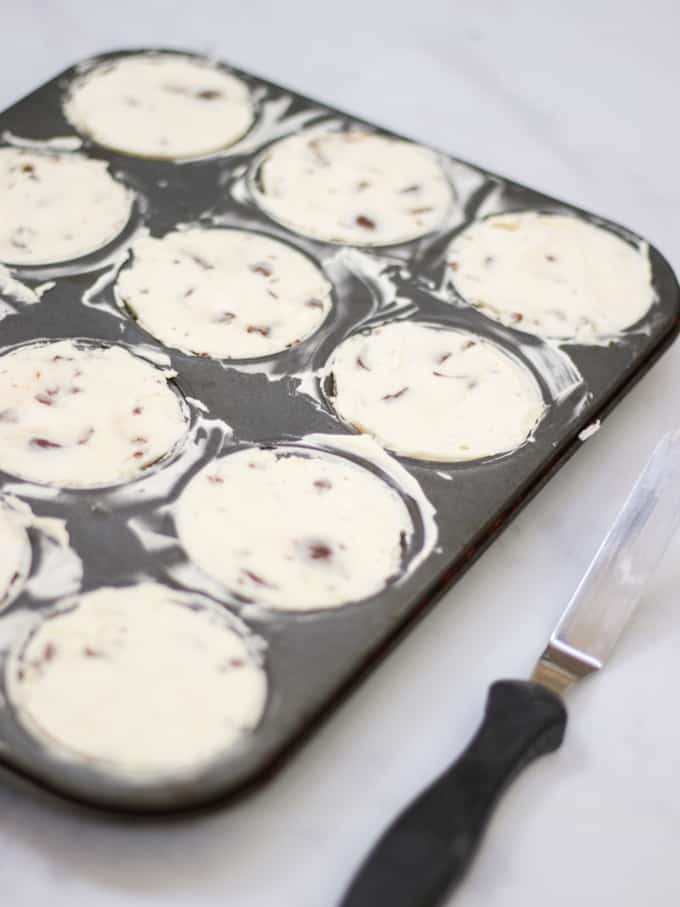 Mini cheesecakes in a muffin tin with angled palette knife on marble background.