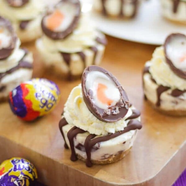 Mini Creme Egg Cheesecakes with cut creme egg on top on a wooden board.