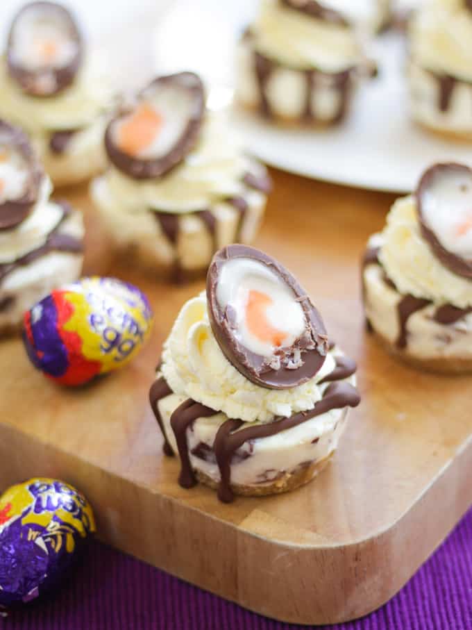 No Bake Mini Creme Egg Cheesecake with cut creme egg on top on a wooden board.