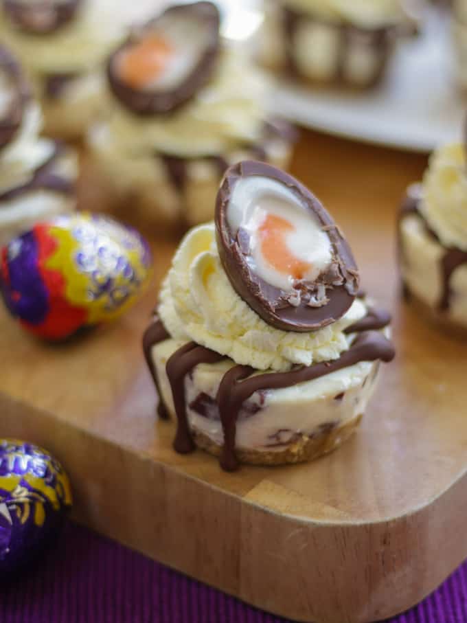 Mini no bake cheesecake topped with a creme egg on a wooden board with creme egg in wrapper.